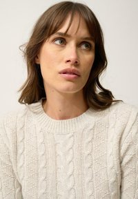 Jasno beżowy sweter z plecionką w sploty, z okrągłym dekoltem i ściągaczami, z teksturowanymi detalami i miękkim wykończeniem materiału.