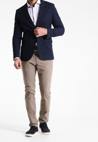 Marinblå kavaj med slim fit och slagkrage, i kombination med ljusbeige byxor och marinblå sneakers. Slät tyg, minimal detaljer.