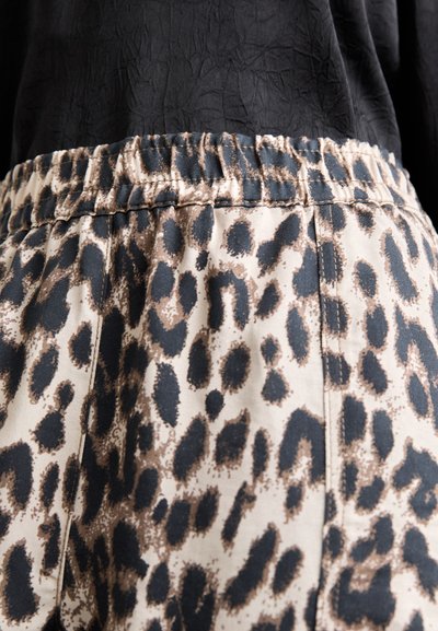 Hlače z elastičnim pasom imajo leopardji vzorec v odtenkih bež, rjave in črne barve. Tkanina ima gladko teksturo z rahlim sijajem.
