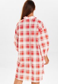 Robe chemise à carreaux rouges et blancs avec un col à boutons et des manches longues. Présente une coupe ample et des fentes sur les côtés pour un confort de mouvement.
