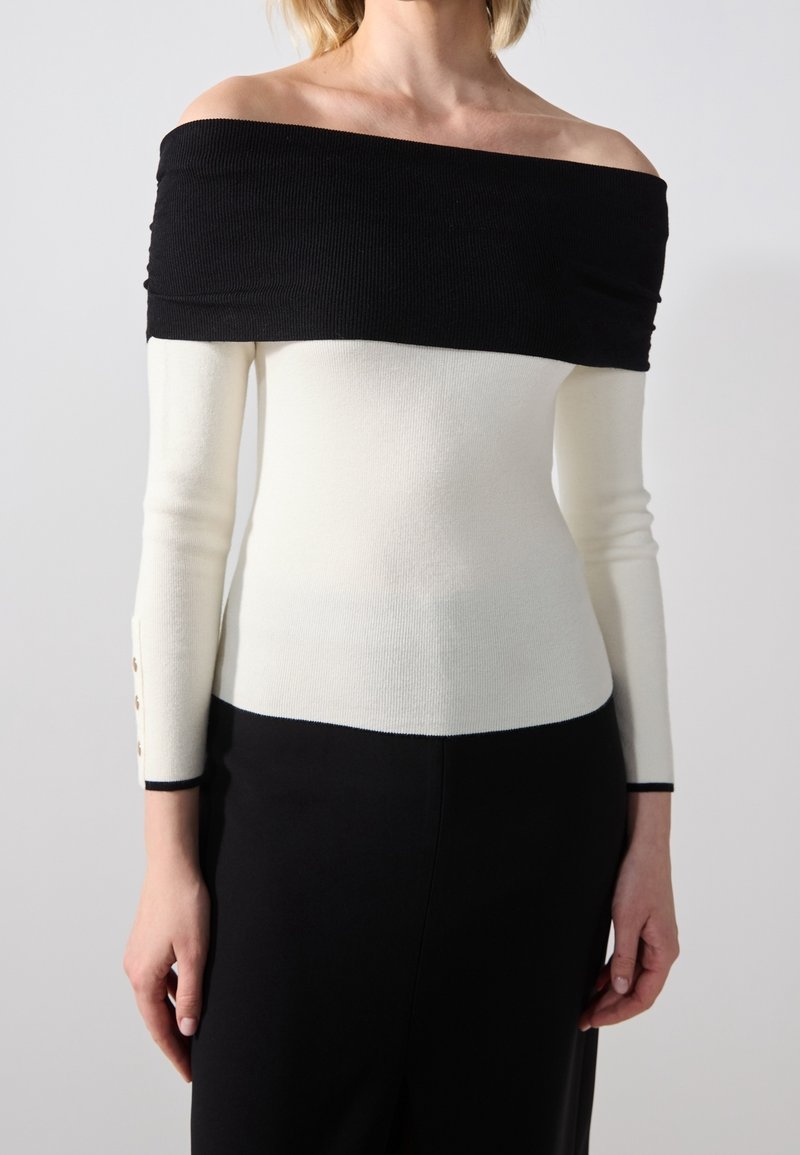 Off-the-shoulder top with black and white color block design, ribbed texture, and button accents at the cuffs. Slim fit and long sleeves.