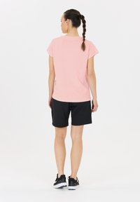 Roze T-shirt met korte mouwen en zwarte shorts, gedragen met zwarte sportschoenen. Het T-shirt heeft een losse pasvorm en een gladde textuur.