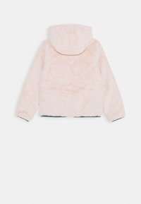 Faux furjakke i lys lyserød med hætte; har en blød tekstur, elastiske manchetter og en kant, der kurver let i bunden.