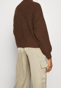 Brązowy, teksturowany sweter dzianinowy o skróconym, luźnym kroju i prążkowanych mankietach, w połączeniu z beżowymi spodniami cargo w szerokim kroju z bocznymi kieszeniami.