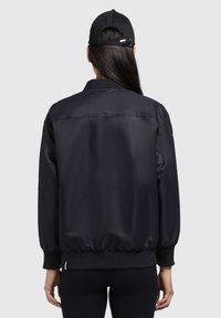 Must must jacket, mille pehmeast polüestrist viimistlusega, ribaga mansetid ja äär. Omab lukku ja küljetaskuid, disainitud lõdva istuvusega.