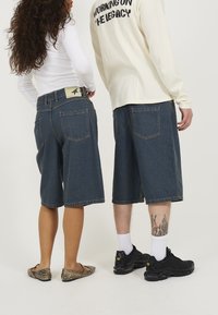 Shorts de mezclilla en azul oscuro con un corte recto, que cuentan con cinco bolsillos, un parche de marca en la cintura y un dobladillo deshilachado. Combinados con calzado en contraste.