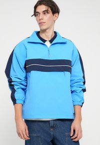 Ανοιχτό γαλάζιο πουκάμισο με μισό φερμουάρ και ναυτικές οριζόντιες ρίγες, ελαστικές μανσέτες και απαλό υφή. Σπορ σχέδιο.