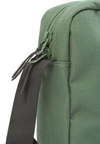 Nahaufnahme einer grünen Stofftasche mit Reißverschluss und schwarzen Riemendetails, die Textur und Materialqualität betont.