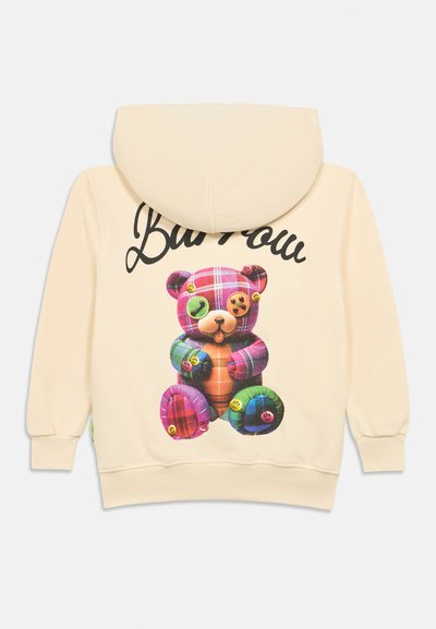 Sweatshirt bege com um gráfico de urso de peluche em patchwork colorido e texto em cursiva preta nas costas.