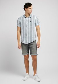 Camisa de botones de mangas cortas con rayas verticales azules y blancas, combinada con pantalones cortos de mezclilla gris y zapatillas blancas.