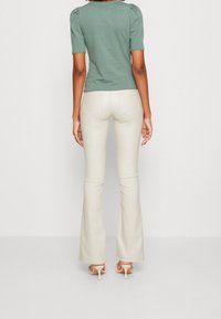 Grön topp med puffärmar som är parat med krämfärgade utsvängda byxor, med bakfickor och en kroppsnära silhuett. Slät textur, neutrala toner.