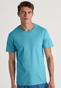 Turquoise kortemouwen t-shirt van zachte stof, met een ronde halslijn en een relaxte pasvorm, gedragen over gevoerde blauwe zwembroeken.