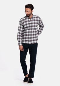 Gekaatst button-up shirt in grijs, wit en bruin, gecombineerd met zwarte slim-fit broek en zwarte instapschoenen. Soepele stof, casual ontwerp.