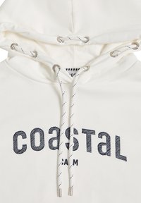 Sweat-shirt à capuche blanc avec texte brodé en bleu marine "COASTAL" et "CALM." Comprend des œillets argentés et des cordons blancs avec des rayures noires.