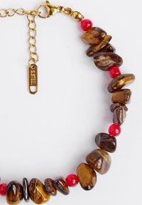 Bruine en rode kraal collier met gepolijste stenen en glanzende rode accenten. Voorzien van een vergulde sluiting en verlengkettinkje met een label.