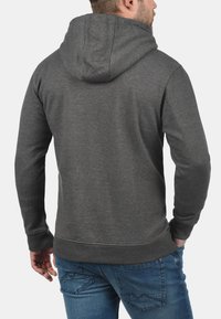 Grijze hoodie met een gestructureerde stof, zichtbare naden, ribgebreide manchetten en zoom. Draagt met blauwe spijkerbroek met een gestikt patroon.