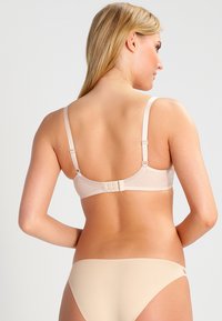 Beige bh med justerbara axelband och hyskor. Slät textur och enkel design utan mönster eller utsmyckningar.