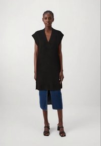 Mustat neulotut tunikat V-päällyksellä, hihattomilla hihoilla ja ribatulla helmalla. Yhdistetty keskikokoiseen farkkuhameeseen, jossa on etureikä. Mustat korkeat sandaalit.