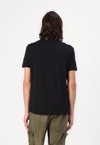 Zwarte t-shirt met korte mouwen en ronde hals, gemaakt van zachte stof, gecombineerd met groene corduroy broek met cargozakken.