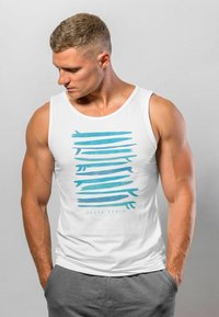 Weißes Tanktop mit blauen horizontalen Streifen und dem Aufdruck "SOUTH BEACH" am unteren Rand. Glattes Material, lockere Passform.