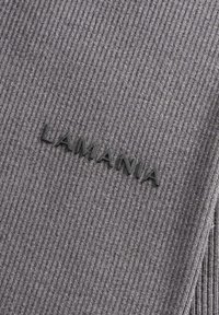 Sivá ribbovaná tkanina s textúrovaným povrchom, na ktorej je výrazne zobrazené čierne logo "LAMANIA".