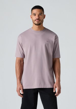 Licht lavendelkleurig katoenen t-shirt met korte mouwen, ronde halsontwerp en een klein logo op de borst, gecombineerd met zwarte broek.