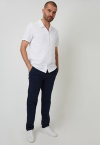 Camisa blanca de botones de manga corta con cuello, combinada con pantalones azul marino y zapatillas blancas. Tejido suave y ajuste clásico.