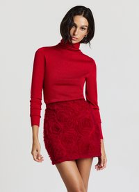 Pull à col roulé rouge avec une texture scintillante, associé à une jupe mini rouge avec des appliqués floraux, présentant des motifs de roses en relief et une silhouette ajustée.