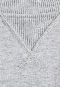 Jasnoszary dzianinowy materiał o fakturze prążkowanej. Charakterystyczne przeszycia tworzą w materiale wzór w kształcie krzyża.