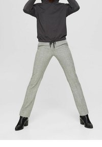 Pantaloni grigi chiari con texture e vita con cordino, abbinati a un top aderente nero a maniche lunghe e stivali neri con tacco alla caviglia.