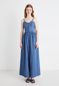 Denim maxikjole med tynne stropper, knappelukking foran, tettsittende bodice og utsvingt skjørt. Lys blå farge, glatt tekstur, uformelt design.