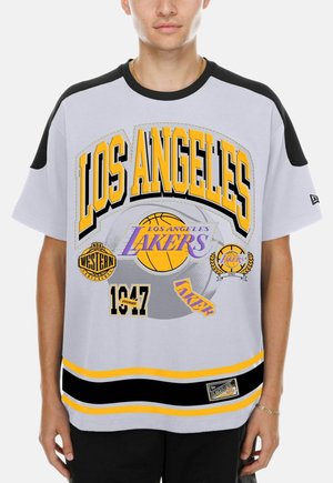 Personne portant un t-shirt gris et noir des Los Angeles Lakers avec des logos jaunes et violets et texte, y compris "LOS ANGELES" et "1947 Founded."