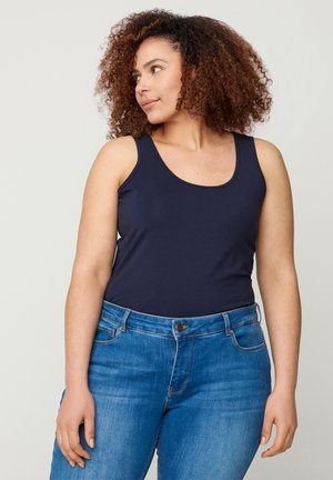 Canottiera blu navy con scollo a barca, realizzata in tessuto morbido, abbinata a jeans blu con chiusura con bottone e design a cinque tasche.