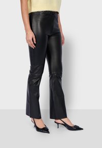 Zwarte leren flared broek met een hoge taille en voornaaddetails, gecombineerd met zwarte spitse slingback hakken.