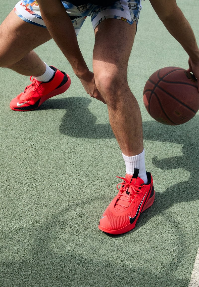 Personne portant des chaussures de basket Nike rouges dribbles un ballon de basket sur un terrain extérieur avec une surface verte texturée.