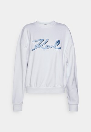 Sweatshirt blanc avec encolure et poignets côtelés, présentant un logo "Karl" brodé en bleu dans une police script sur le devant.