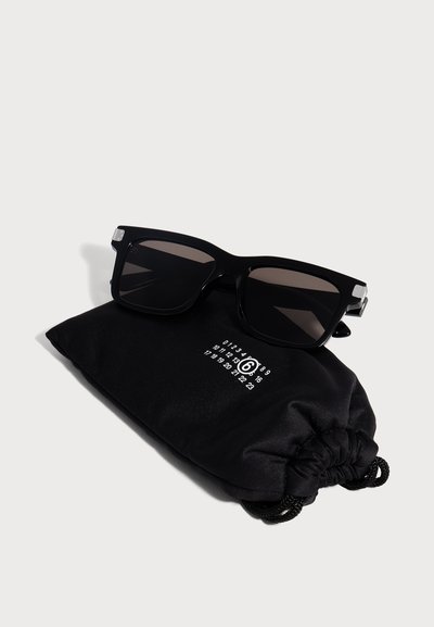 Lunettes de soleil noires rectangulaires posées sur une pochette noire à cordon avec des chiffres blancs imprimés sur un fond clair.