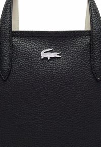 Sac à main en cuir texturé noir avec un détail de logo crocodile en argent. Le design comprend deux poignées supérieures pour plus de commodité lors du transport.