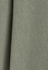 Gros plan sur un tissu tricoté côtelé vert olive plié montrant une texture douce et un motif tricoté vertical.
