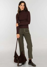 Jersey marrón de cuello alto con textura acanalada, pantalones verdes a cuadros con ribetes, bolso de ante oscuro y mocasines oscuros en un entorno neutro.