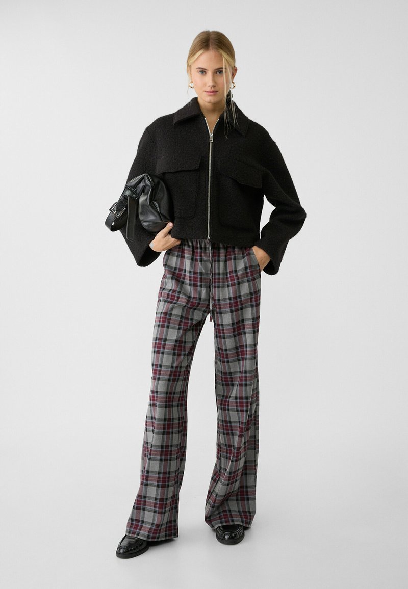 Czarna, krótka kurtka z wełny mieszanej z dwoma przednimi kieszeniami, w parze z szerokimi spodniami w szary kratkę z burgundowymi akcentami. Czarna torba i buty.