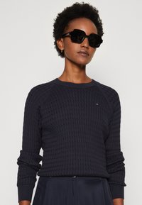 Maglione a girocollo della marina con motivo testurizzato, polsini a coste e piccolo logo decorativo. Gli occhiali da sole oversize neri completano il look.