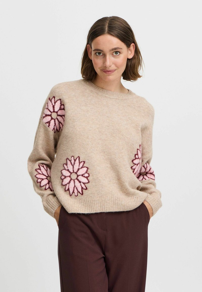 Pull en laine beige avec des motifs floraux roses et bourgogne foncé sur les épaules. Encolure ronde et poignets côtelés, coupe décontractée.