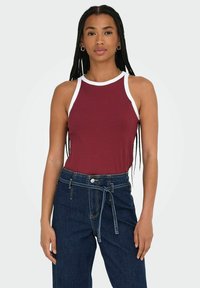 Top sin mangas de canalé burdeos con ribetes blancos, combinado con jeans oscuros de cintura alta que cuentan con un cinturón atado y cierre frontal de botones.