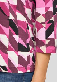 Multicolored top featuring a geometric pattern in shades of pink, black, and cream; made of stretchy fabric with a round neckline and cuffed sleeves.