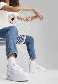 White platform sneakers with light grey and pink accents, worn with blue denim jeans and white socks, paired with a graphic T-shirt.