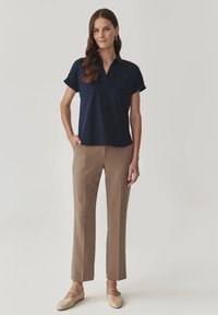 Marineblauwe polo met opgerolde mouwen, gecombineerd met lichtbruine op maat gemaakte broeken en beige ballerina's. Eenvoudige, strakke lijnen en een moderne pasvorm.