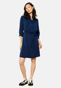 Robe chemise bleu marine avec col, fermeture à boutons sur le devant, ceinture à nouer à la taille et manches trois-quarts. Fabriquée dans un tissu doux et avec une coupe décontractée.