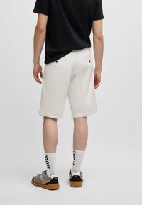 Shorts en coton blanc avec poches arrière et boutons noirs, accompagnés d'un t-shirt noir et de baskets grises. Chaussettes blanches avec le texte "HUGO".