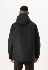 Μαύρο μπουφάν με κουκούλα, με υφή στην επιφάνεια. Διαθέτει χαλαρή, φαρδιά εφαρμογή και απαλές ραφές. Μινιμαλιστικός σχεδιασμός χωρίς ορατά εξαρτήματα.